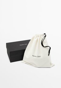 Boîte rectangulaire noire Massimo Dutti à côté d'une pochette en tissu blanc à cordon noir avec le logo Massimo Dutti.