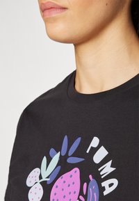 Czarny bawełniany T-shirt z okrągłym dekoltem, zdobiony kolorową grafiką owoców i liści w odcieniach purpury, różu i jasnoniebieskiego.