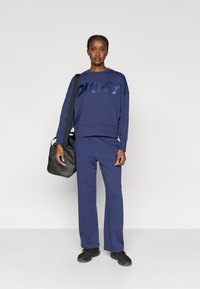 Tmavě modrá bavlněná mikina s logem "DKNY", doplněná o ladící široké kalhoty. Černá kabelka přes rameno a tenisky dokončují outfit.