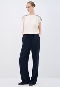 Blusa color crema con spalle impreziosite, abbinata a pantaloni larghi blu navy in tessuto trapuntato. Calzature casual incluse.