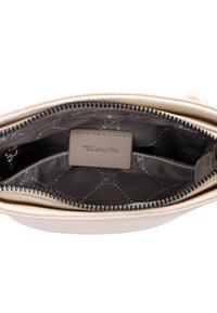 Intérieur d'un sac à main synthétique beige avec doublure à motifs gris, fermeture zippée et compartiments pour l'organisation. Étiquette avec "Tomaris" visible.