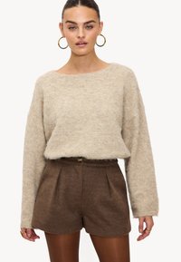 Pull beige en maille avec un large décolleté et une coupe ample, associé à un short en laine marron taille haute avec des plis à l'avant.