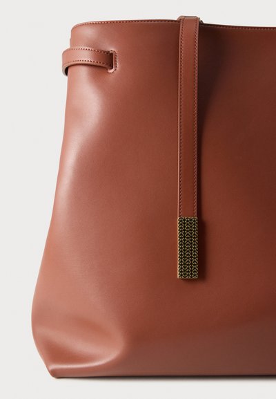 Καφέ δερμάτινη τσάντα ώμου με ομαλή υφή. Διαθέτει μακρύ, λεπτό λουρί και διακοσμητικό μεταλλικό στοιχείο με γεωμετρικό σχέδιο.