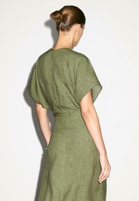 Abito in lino verde oliva con una vestibilità rilassata, maniche corte a dolman e una vita aderente, che mette in risalto un tessuto texture.