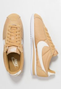 Nike-sneakers i beige och kräm. Canvas- och mockamaterial, rundad form, med platta snörningar, vit sula och klassisk swoosh-logotyp.