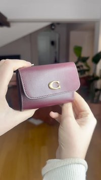 Tumepunane nahast rahakott kuldse logoga, millel on klapiga sulgur, õmmeldud detailid ja kompaktne ristkülikukujuline vorm.