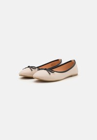 Ballerinaskor i beige läder med svarta detaljer, spetsig tå och liten rosett fram. Inuti finns en beige foder.