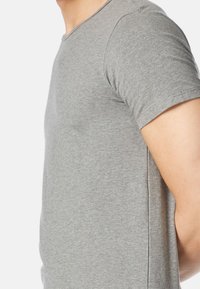 T-shirt grigio a maniche corte realizzato in tessuto morbido e liscio, con scollo rotondo e una silhouette aderente. Dettagli delle cuciture visibili sui lati.