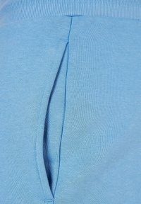 Ljust blå sweatpants i en mjuk, texturerad tyg med en sidficka och en ribbad midja. Designen betonar komfort och funktionalitet.