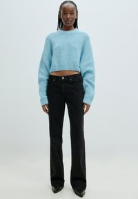 Hellblau gestrickter, verkürzter Pullover mit langen Ärmeln, kombiniert mit hochgeschnittenen, schwarzen, schmal geschnittenen Jeans und schwarzen, spitzen Absätzen.