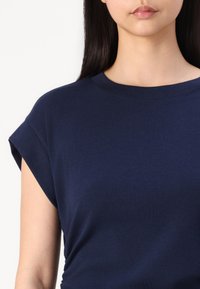 Tamno plavi majica kratkih rukava napravljena od pamuka, s okruglim izrezom i zavrnutim rukavima, s glatkom, teksturiranom površinom.