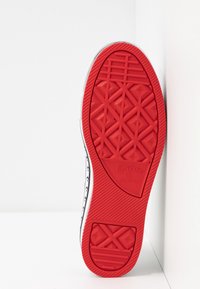 Röd gummisula på en Converse-sko, med ett geometriskt mönster, texturerad yta och varumärkesnamnet präglat på hälen.