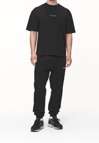 Černé tričko s modrým logem "PEGADOR" v kombinaci s černými tepláky. Oblečení má volný střih a pohodlnou tkaninu.