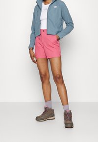 Jasnoniebieska polarowa kurtka na zamek, biała koszulka, różowe szorty i szare buty trekkingowe z różowymi akcentami. Miękka faktura, casualowy styl na świeżym powietrzu.