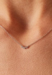 Silberne Kettenhalskette mit drei kleinen, runden, funkelnden Akzenten, gestaltet in einem minimalistischen Design vor einem strukturierten Hauthintergrund.