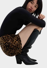 Czarna bluzka z długim rękawem, mini spódniczka w zwierzęcy wzór i czarne skórzane kozaki na wysokim obcasie do kolan. Materiał ma gładką teksturę, a spódniczka jest ozdobiona marszczeniami.