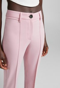 Ljust rosa byxor med en slät textur, utrustade med en enkel knappstängning, framfickor och vertikala sömmar för en skräddarsydd look.