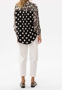 Blusa bianca e nera con motivo paisley sul retro e grandi pois sul davanti. Abbinata a pantaloni bianchi e scarpe con stampa serpente.