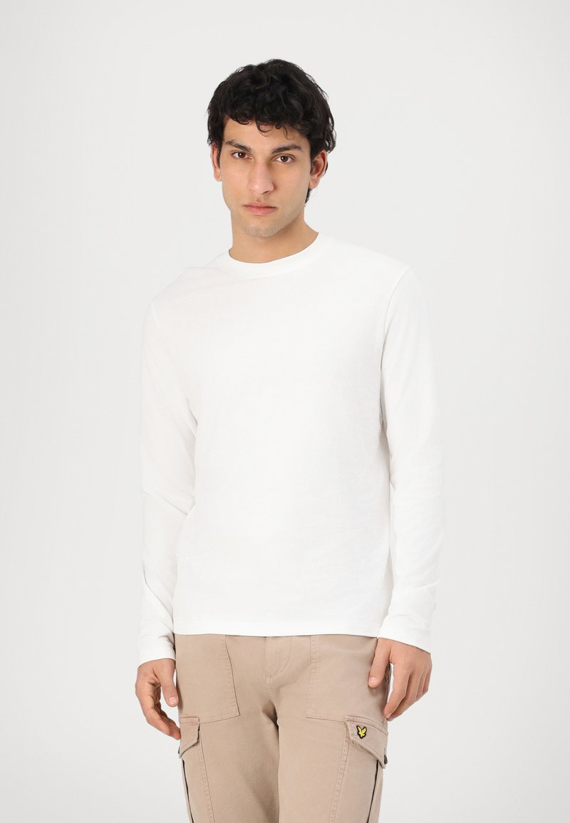 Bílá dlouhá tričko s dlouhým rukávem z měkkého materiálu, kulatým výstřihem, slim fit, s jemnými švy, spárované s béžovými cargo kalhotami.