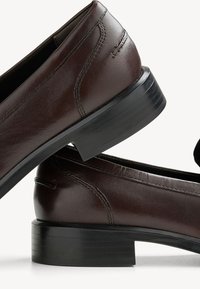 Leather loafers in dark brown with smooth texture, low stacked heel, side stitching detail, and a rounded toe design.