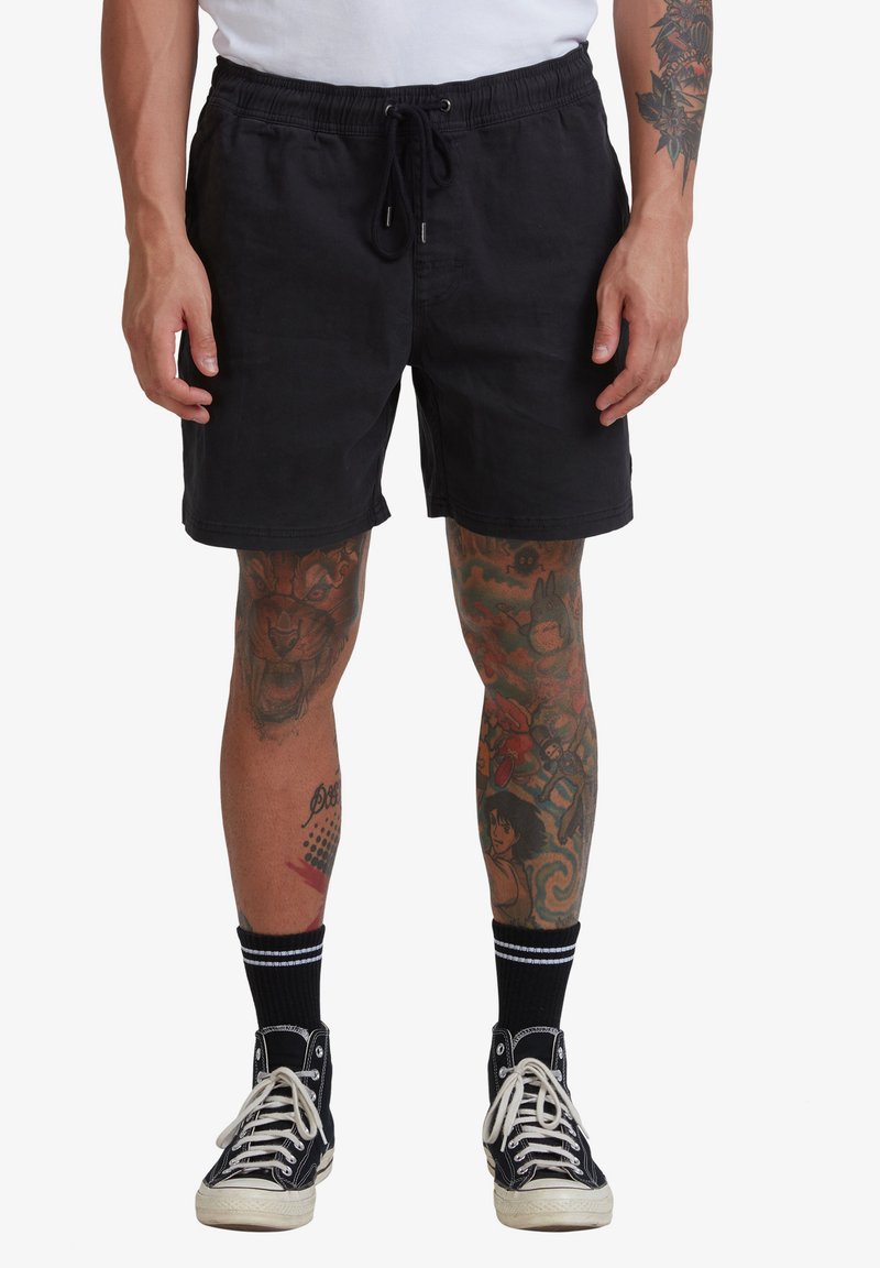 Shorts neri in cotone con vita elastica e cordoncino. Indossati con sneaker alte nere e calzini a righe neri.