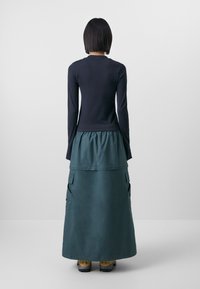 Haut à manches longues bleu marine associé à une jupe maxi turquoise avec des poches cargo. Le tissu semble lisse ; la jupe a une taille froncée.