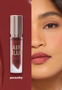 Flytende leppestiftprodukt i en klar tube med metallisk hette; fargen er en myk matt ferskenfarge. Inkluderer fargeprøve og modellens lepper i samme nyanse.