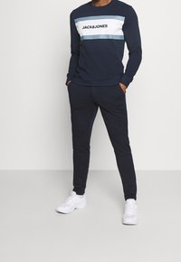 Marineblauwe sweatshirt met witte en lichtblauwe horizontale strepen, voorzien van het "JACK&JONES" logo. Gecombineerd met bijpassende marineblauwe joggers en witte sneakers.