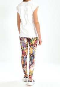 Bílý top bez rukávů s potiskem "13" na zadní straně, doplněný barevnými legínami se vzorem ptáků a květin; černo-bílé tenisky.