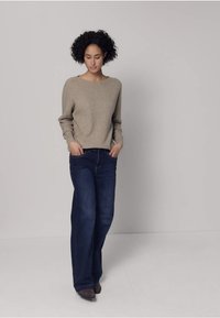 Pull beige en maille avec un col rond associé à un jean large bleu foncé. La tenue présente une coupe décontractée avec des matériaux texturés.