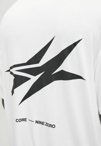 Balta medvilninė marškinėlių su dideliu juodu abstrakčiu dizainu ant nugaros ir tekstu "CORE - NINE ZERO" po grafika.