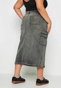 Grå denim midi kjol med rak skärning, med två stora bakfickor och en sidficka. Bärs med svarta sneakers.