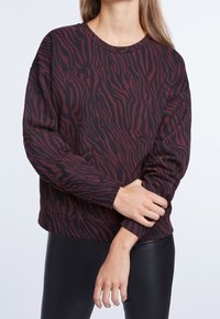 Felpa a righe zebrate marrone e nera con scollo rotondo, maniche lunghe e vestibilità comoda. Il materiale sembra morbido e con una texture interessante.
