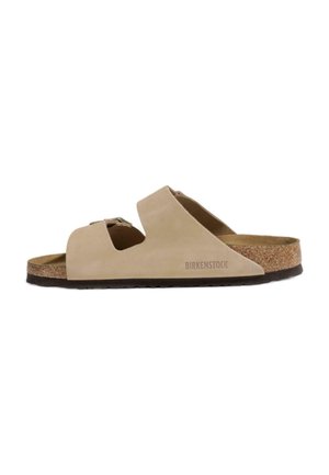 Sandalo beige Birkenstock con due ampie cinghie regolabili, plantare in sughero e suola nera, mostrato di profilo su sfondo bianco.