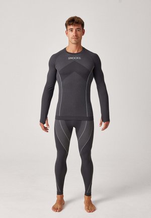Sort atletisk basislagssæt med langærmet top og tætsiddende leggings, der har tekstureret stof og kontrasterende hvide syninger.