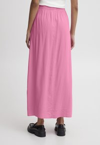 Falda maxi rosa hecha de una tela ligera, con una cintura elástica y una textura suave. Estilizada con zapatos de plataforma negros.