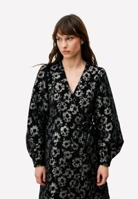 Zwarte jurk met lange mouwen, zilveren bloemmotief, diepe V-hals en tailleceintuur. Gestructureerde stof met een glanzend uiterlijk.