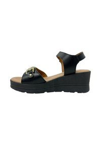 Sandalo con zeppa in pelle nera, con punta aperta, cinturino alla caviglia e decorazioni in oro sulla parte anteriore. La suola nera testurizzata supporta il design.