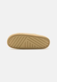 Semelle d'une pantoufle en caoutchouc beige avec un motif de bande de roulement rainurée diagonale et verticale sur fond blanc.