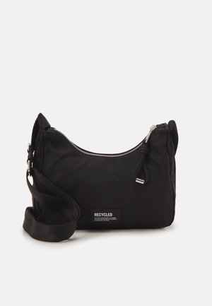 Schwarze Umhängetasche mit verstellbarem Riemen, Reißverschluss oben und einem Etikett mit der Aufschrift "Recycled" auf der Vorderseite.