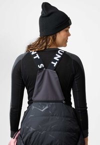 Beanie nera, maglia a maniche lunghe con accenti grigi e un gilet imbottito nero con zip che presenta un motivo geometrico e cinturini con logo.