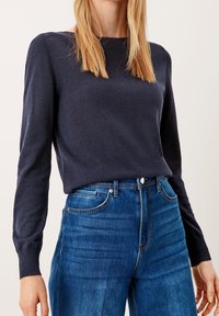 Granatowy sweter dzianinowy z długimi rękawami i prążkowanym dekoltem, zestawiony zjeansami w kolorze niebieskim o wysokim stanie z klasycznym pięciopocketowym fasonem.