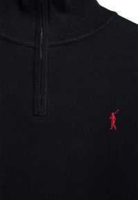 Pull noir en tricot avec une fermeture éclair au quart et un petit logo rouge brodé représentant une personne tenant un maillet de polo sur la poitrine.