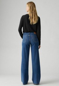 Wijdbenige blauwe jeans van denim met een hoge taille, voorzien van opvallende achterzakken en een leren merkembleem op de tailleband.