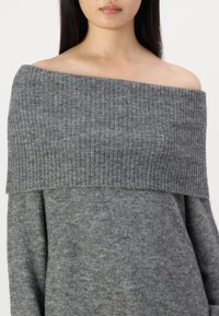 Pull gris à épaules dénudées avec un col côtelé et une texture douce. Présente une coupe décontractée et une subtile variation de nuances de gris.