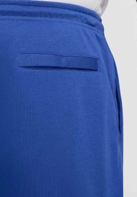 Blå sportshorts av mjukt tyg, med elastisk midjeband och en liten lappficka på baksidan för minimal förvaring.