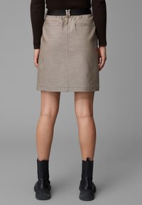 Ruskea houndstooth-kuvioinen hame suoran leikkauksen omaavana, mustalla vyöllä varustettuna ja kahdella takataskulla. Yhdistetty mustiin nilkkabootseihin.