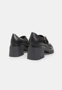 Chaussures en cuir noir avec une semelle épaisse et crantée et un bout pointu. Présente un détail en boucle sur le côté et une texture lisse.