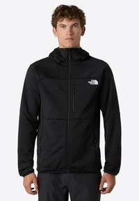 Schwarze Fleecejacke mit Kapuze, Reißverschluss vorne und Brusttasche. Mit einem Logo auf der oberen linken Seite und seitlichen Taschen für Stauraum.