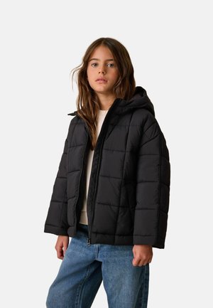 Chaqueta acolchada negra con capucha, con un diseño cuadrado y textura acolchada. Cierre delantero con cremallera y mangas anchas. Llevada sobre una prenda ligera.